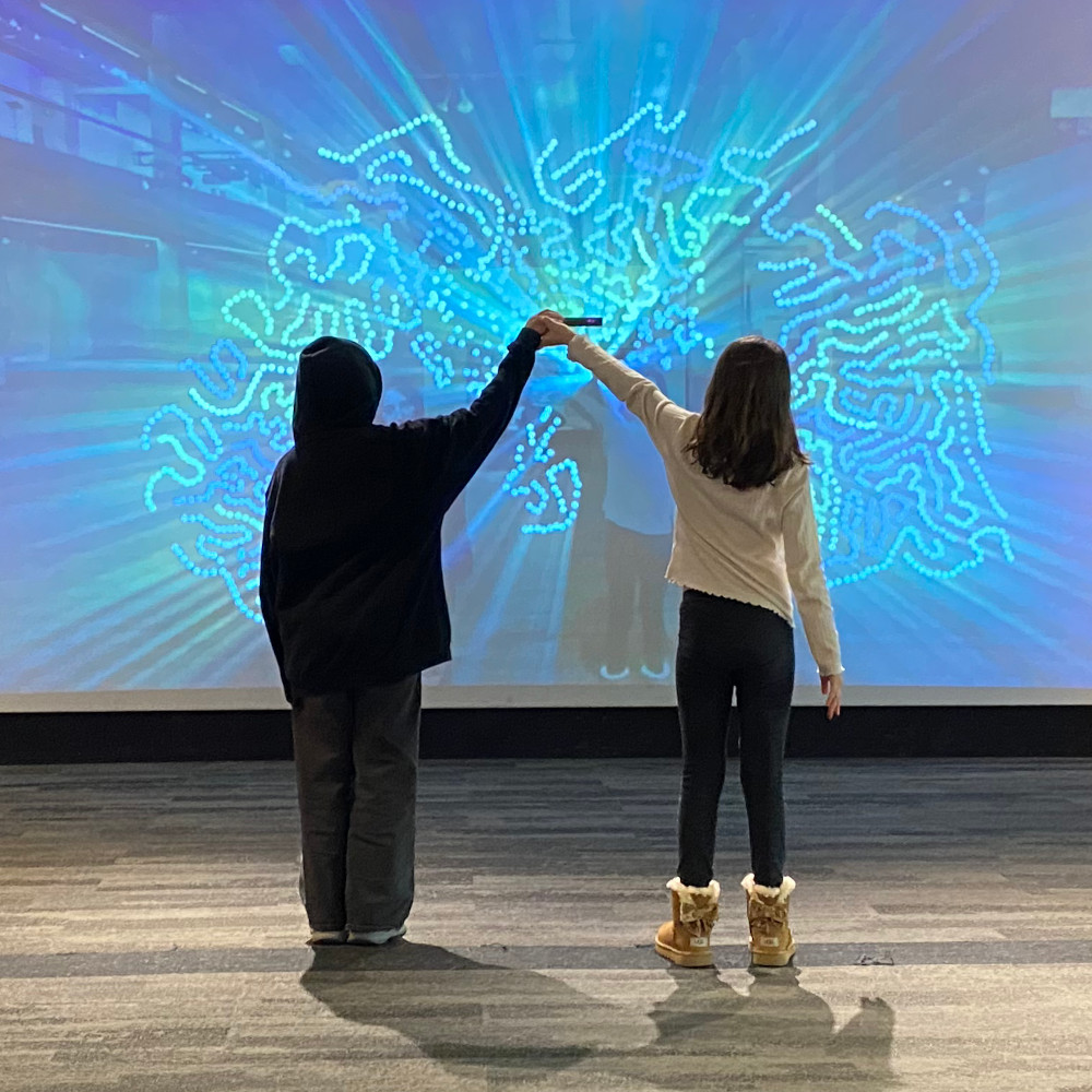Two kids in front of a big interactive screen.